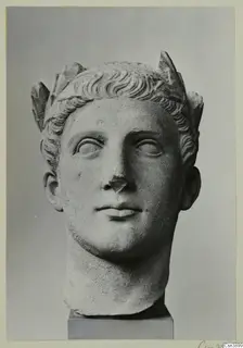 Carved stone head of a figure with curled hair and a leafy headdress, mounted on a square base.