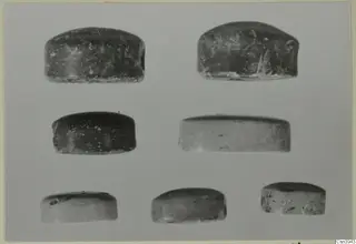 Seven small domed stone objects, dark and pale, arranged in three rows on a grey background, glyptic material