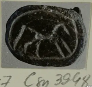 Oval engraved seal of dark stone with a pale incised design, mounted on a grey card