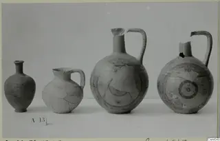 Four pottery vessels of different sizes standing in a row on a pale surface, the two on the right with painted bands and concentric circles