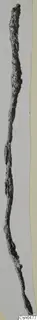 Long, thin corroded iron object standing upright against a pale background