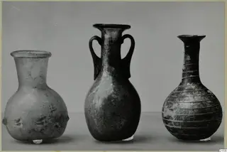 Three blown glass vessels in a row: a flared-rim bottle, a two-handled vessel and a ribbed bottle with a long neck