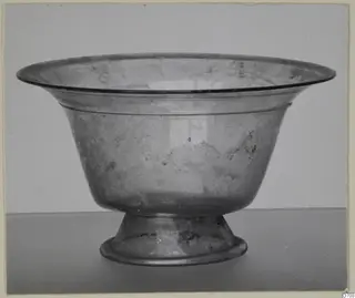 Blown glass bowl on a stemmed foot, with a flared rim, photographed against a grey backdrop.