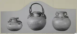 Three blown glass vessels with handles, shown side by side on a grey mount
