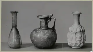Three small vessels in a row: a slender bottle, a round jug with a loop handle, and a white vessel with moulded relief panels