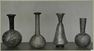 Four blown glass bottles with long necks, standing in a row on a dark surface.