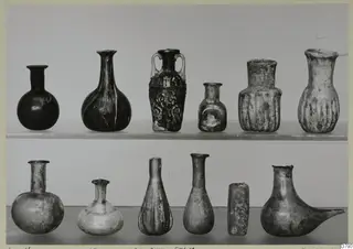 Twelve small blown glass vessels arranged in two rows on shelves