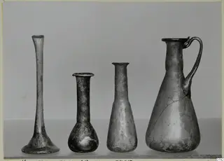 Four blown glass vessels in a row: three slender vases or bottles and a jug with a looped handle.
