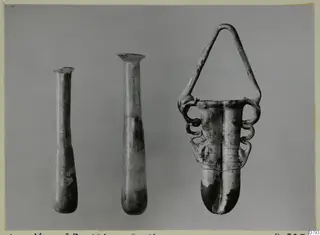 Three glass vessels side by side: two tall slender bottles and one with an arched looped handle.