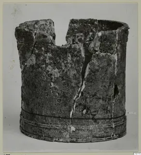 Cylindrical bone object with a broken, uneven rim and grooved bands near the base, photographed against a grey backdrop.