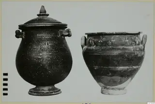 Two clay vessels: a covered jar with a knob lid and handles, and a wide jar with painted vine decoration.