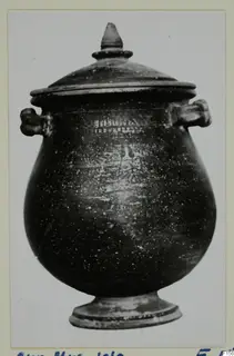 Dark covered vessel with two side handles and a footed base, shown on a mounted photograph card