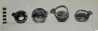 Four black-glazed vessels in a row beside a striped scale bar, with handles and spouts