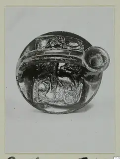 Single round dark glossy vessel with a tubular spout and relief decoration, shown on a mounted print