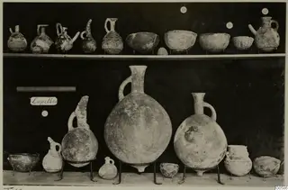 Jugs and bowls from Lapithos Markides, T.12, set out on two shelves against a dark background