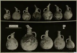 Rows of round juglets with long spouts and loop handles against a dark background, from Lapithos Markides T.49.