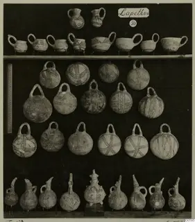 Jugs, cups, bowls and round flasks from Lapithos, T.50, arranged in rows on a dark board