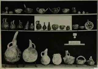 Jugs, bowls and flasks from Lapithos Markides, tomb 201, set out on three shelves against a black background