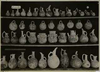 Jugs and juglets from Lapithos Markides T.29, arranged on three shelves against a dark background.