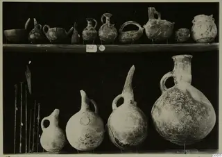 Pottery jugs, juglets and bowls from Lapithos Markides on two shelves against a dark background