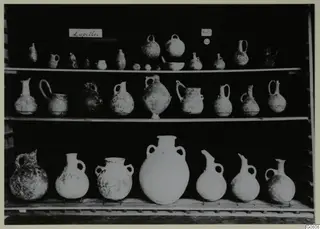 Jugs and bowls from Lapithos Markides, T.14 E, arranged on three shelves against a dark background