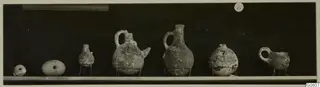 Row of small pottery vessels on a shelf, one with a painted pattern, from Lapithos Markides T.39