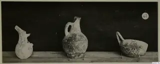 Three pottery vessels from Lapithos Markides, T.42, on a wooden shelf: a broken jug, a handled jug and a painted handled bowl.