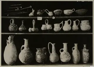 Pottery jugs, bowls and metal objects from T.4 at Lapithos Markides, arranged on three shelves