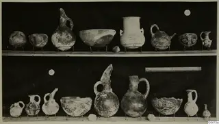Pottery vessels from Lapithos Markides T.46B-e, shown in two rows on small wire stands against a dark background