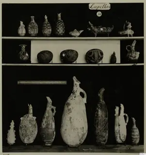 Pottery jugs, juglets and bowls from Lapithos Markides T.50, arranged on three shelves against a black background