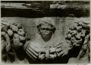 Carved stone relief of a human head between garland swags and draped folds, from a sarcophagus