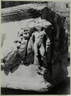Carved relief on a pale stone block, with a small nude figure among clusters of fruit and drapery folds