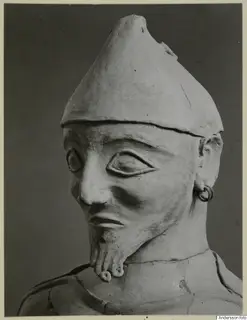 Terracotta statue of a bearded figure in a pointed conical cap, shown head and upper body.