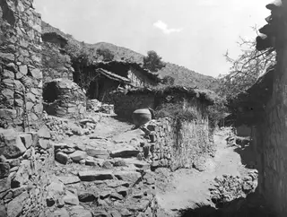 Stone-walled village lane with a stepped path and a large earthenware jar on a low wall