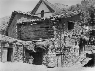 Stone-walled village buildings with tiled and thatched roofs in Lazania, with a figure standing in a doorway
