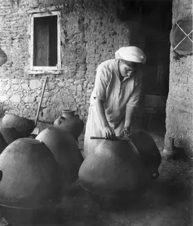 Woman in a headscarf polishing a large clay jar at Klirou, with more jars standing around her