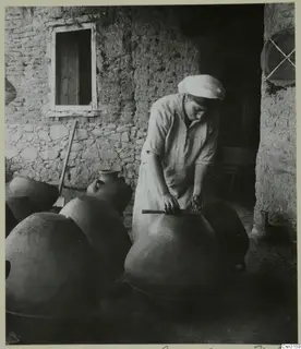 Pottery making at Klirou: a person polishing a large jar with a wooden stick in a farmyard