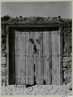 Wooden plank door with iron studs, carved frame and ring knocker set in a stone and earth wall
