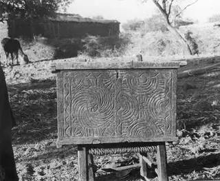Carved wooden chest on a wooden stand outdoors, its front panel decorated with concentric circles and rosettes