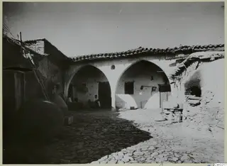 Cobbled courtyard at Klirou with two arched openings, a leaning ladder and large jars