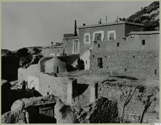 Village houses of mud-brick and stone at Mandres, with people on steps and a low domed structure in the middle
