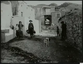 Village street at Lindros with whitewashed and stone houses, five people and a dog