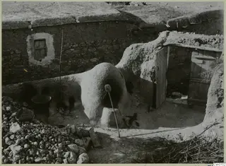 Domed clay bread oven beside a stone-walled house with a wooden door, at Mándres