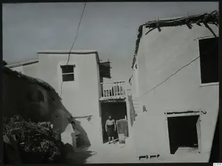 Whitewashed houses around a courtyard at Mándres, with a man standing in a doorway.