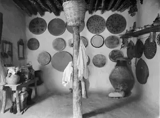 Interior of a house with round woven baskets hung on the mud-plastered walls and a large jar standing by the wall