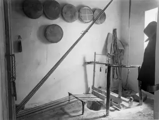 Interior of a room at Milia with a wooden loom set against a whitewashed wall, with round objects hung above it.