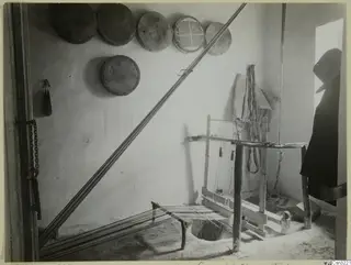 Wooden loom in a whitewashed room at Milia, with round sieves hung on the wall