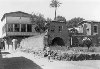 Street in Nicosia with a shuttered upper-floor building, an arched arcade and a standing person