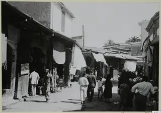 Street in Nicosia lined with shop fronts, white cloths hanging from awnings, and people walking in the road.