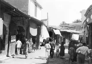 Street in Nicosia lined with shopfronts and hanging white cloths, with people walking along it